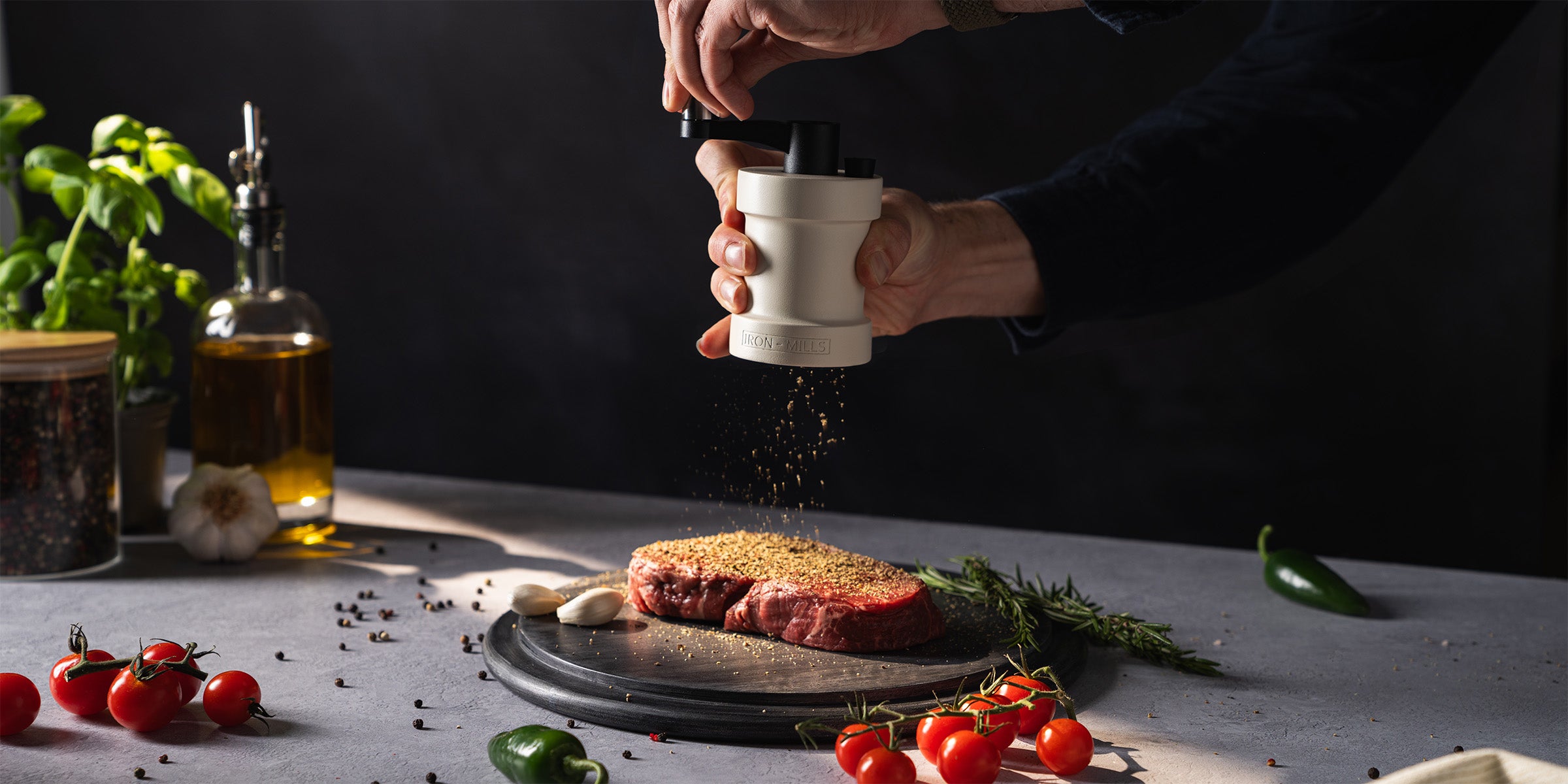 The Oyster White Iron-Mills salt and pepper mill seasoning a fresh steak – handcrafted cast iron precision for the heart of your kitchen.