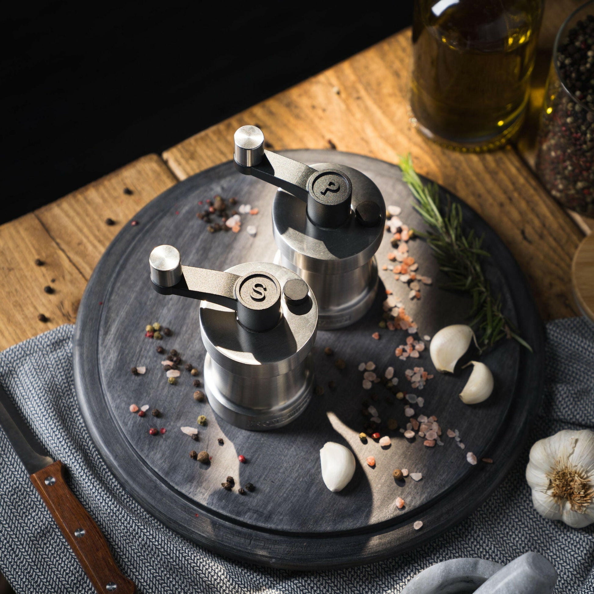 Iron-Mills brushed stainless steel salt and pepper mills on a chopping board in a sleek modern kitchen with condiments nearby