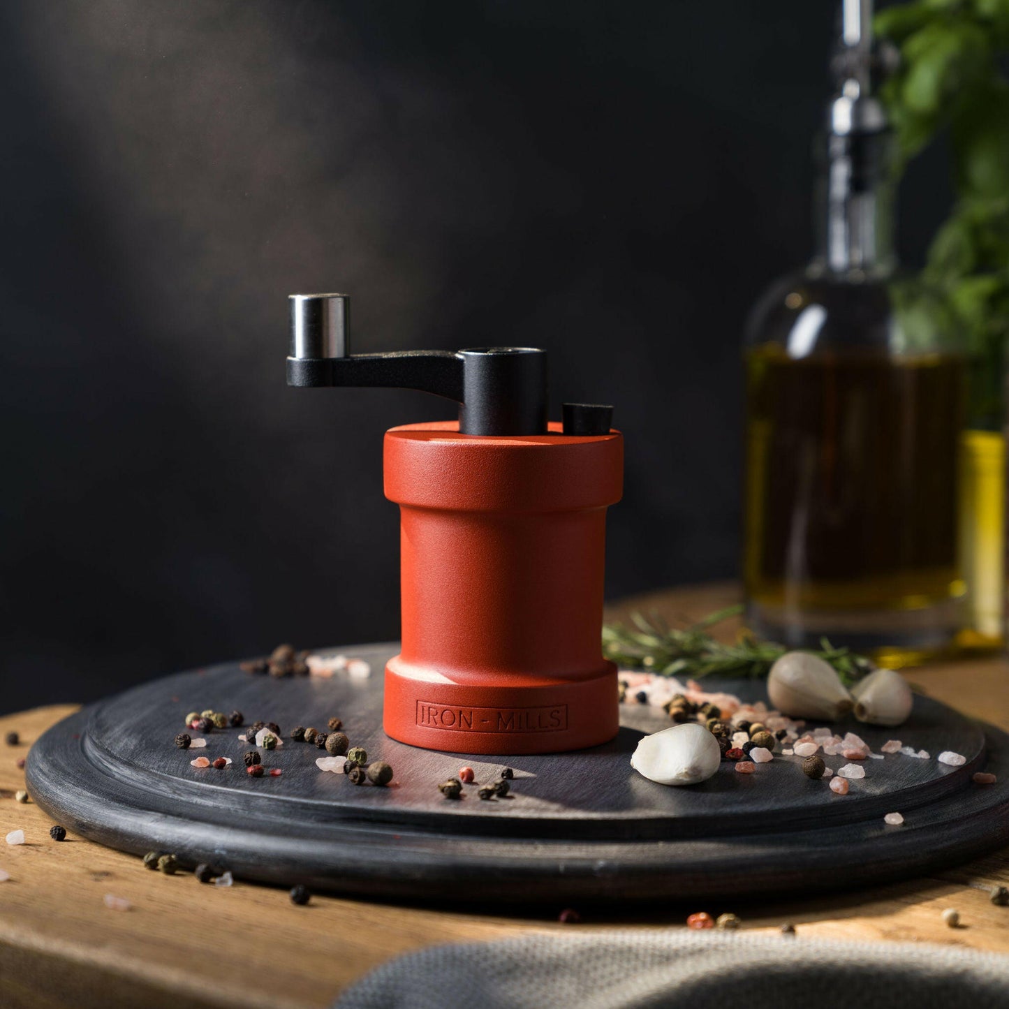 Iron-Mills coral red salt mill on a chopping board in a vibrant kitchen setting with peppercorns